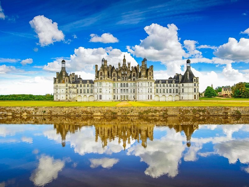Château de Chambord across the water, its roofline of towers and chimneys reflected under a blue sky